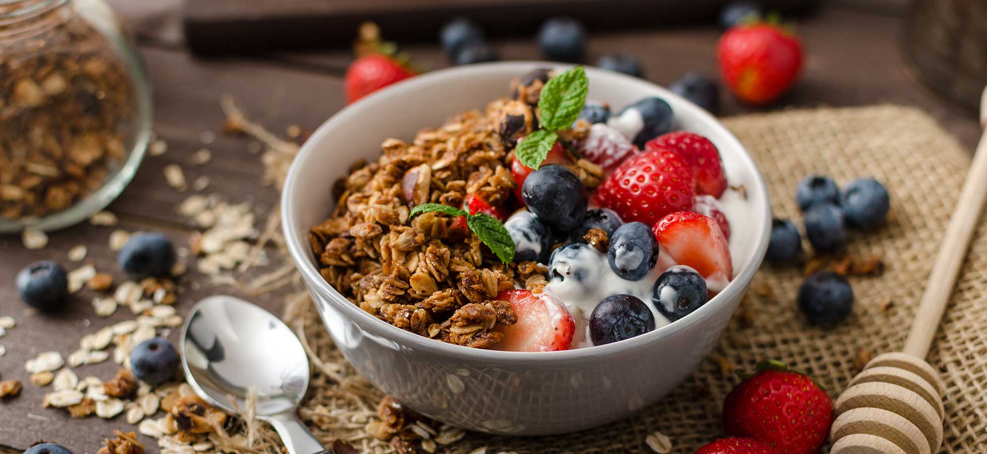 Eine Schüssel Müsli, garniert mit Erdbeeren, Blaubeeren und einem Zweig Minze, auf einer Holzoberfläche platziert.