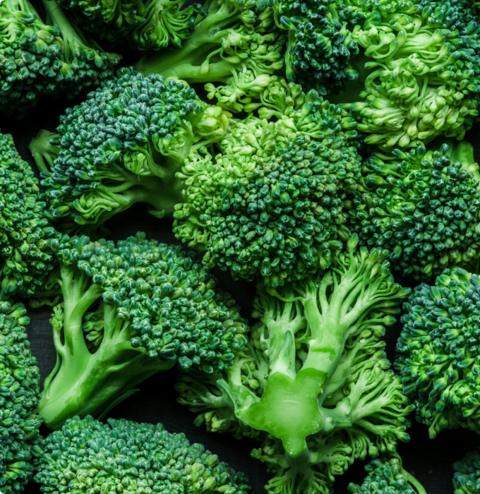 Eine Ansammlung frischer Brokkoliröschen in verschiedenen Grüntönen, die nah beieinander liegen. Die Röschen sind dicht und stark strukturiert, mit feinen Blättern und Stielen sichtbar. Die gesamte Szene vermittelt Frische und gesunde Ernährung.