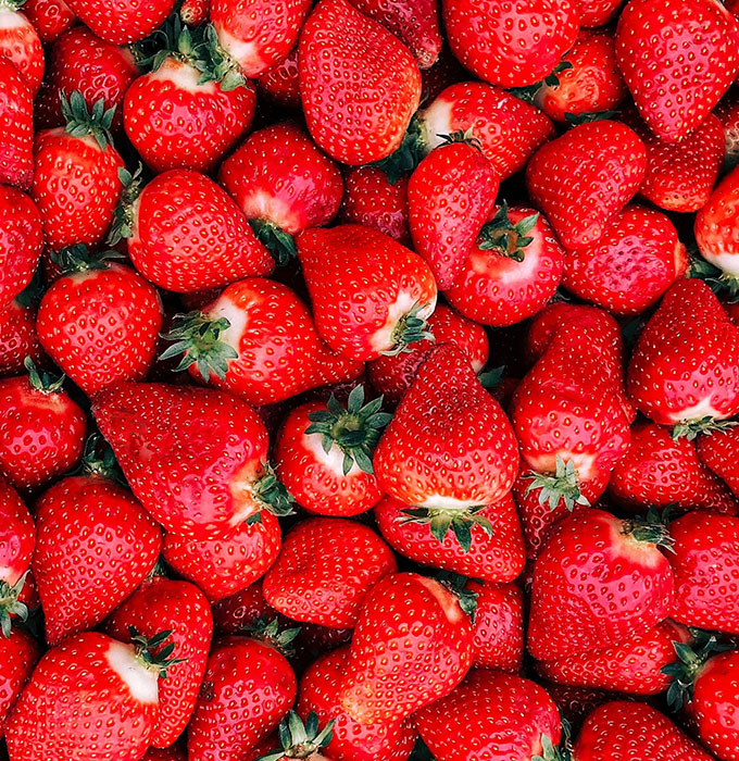 Eine volle Ansammlung von frischen, roten Erdbeeren mit grünen Kelchen. Die Erdbeeren sind in verschiedenen Größen und Formen, eng beieinanderliegend, was ein lebendiges und saftiges Bild vermittelt.