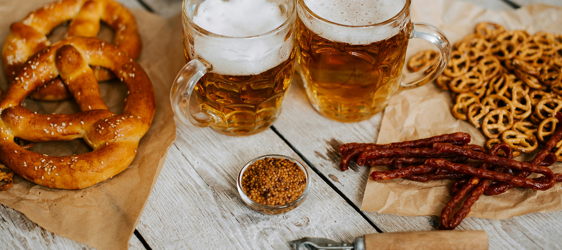 Ein rustikales Essen auf einem Holztisch. Links ein Teller mit zartem Fleisch und frischen Kräutern, daneben ein kleiner Salat. Rechts ein großes Stück knuspriger Schweinshaxe, umgeben von grünem Salat und gebratenen Kartoffeln. Im Hintergrund ist ein Glas mit Eiswürfeln zu sehen.